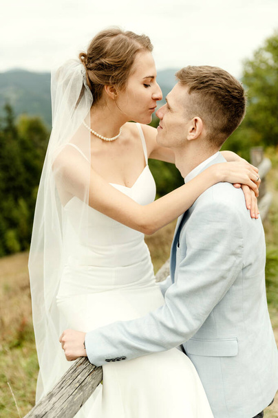 Beautiful newlyweds hug and smile being in nature. Portrait of the bride and groom in a lace dress. Wedding day of a happy couple of newlyweds. couple in the mountains - Fotoğraf, Görsel