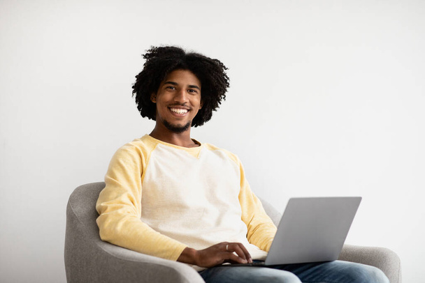 Távoli Karrier. Mosolygó fekete srác laptoppal ül a karosszékben otthon - Fotó, kép