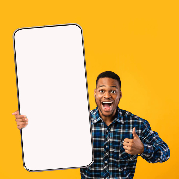 Király mobil alkalmazás. Elégedett fekete férfi bemutató mobiltelefon üres képernyőn, mutatja hüvelykujj fel gesztus, mockup - Fotó, kép
