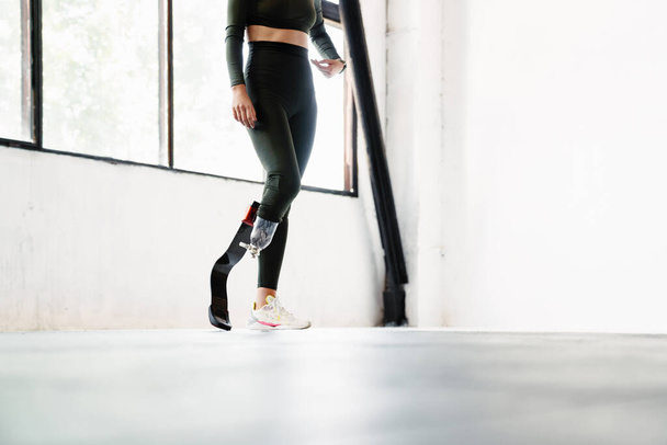 Young woman with prosthesis standing while working out indoors - 写真・画像