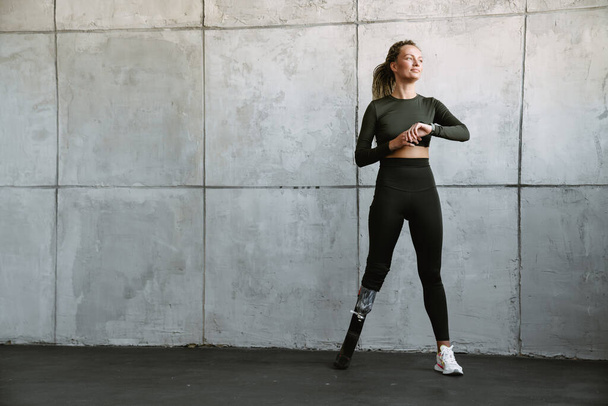 Young sportswoman with prosthesis using smartwatch while working out indoors - Fotoğraf, Görsel