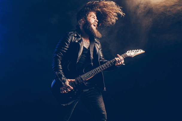 Emotional man rock guitar player with long hair and beard plays on the smoke background. Studio shot - Foto, Imagem