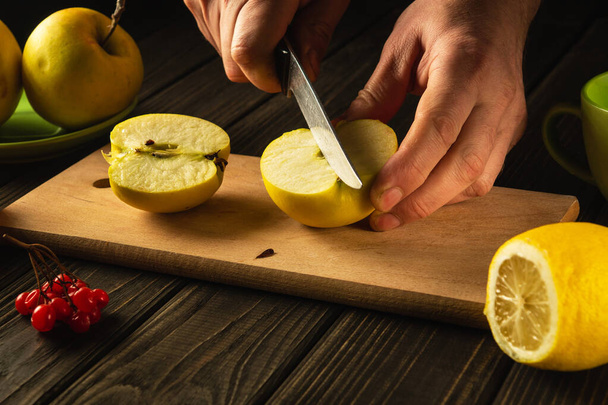 Haciendo mermelada de manzana en casa. Las manos de un cocinero con un cuchillo cortando manzanas frescas en una tabla de cortar. La ración de frutas para el juego de las vitaminas - Foto, imagen