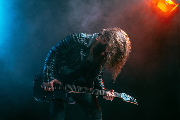 Emotional man rock guitar player with long hair and beard plays on the smoke background. Studio shot - Foto, Bild