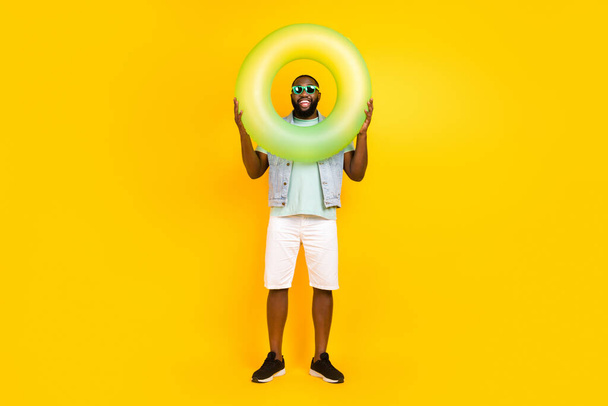 Full length body size view of attractive trendy cheerful guy holding life buoy having fun isolated over bright yellow color background - Foto, afbeelding
