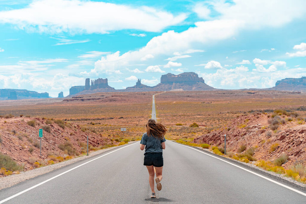 Attractive young woman from back view running in the middle of American straight road in the desert. - Fotoğraf, Görsel