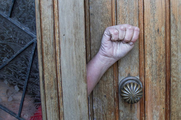 violenza domestica, chiedendo aiuto, la mano di una donna fa un segno chiedendo aiuto da una porta chiusa, dal palmo della mano alla fotocamera e al pollice rimboccato - Foto, immagini