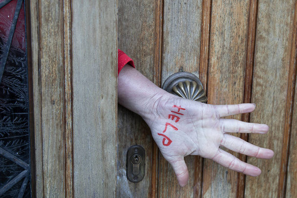 violenza domestica, chiedendo aiuto, la mano di una donna fa un segno chiedendo aiuto da una porta chiusa, dal palmo della mano alla fotocamera e al pollice rimboccato - Foto, immagini