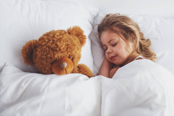 Douce petite fille dort avec son ours en peluche au lit à la maison
 - Photo, image