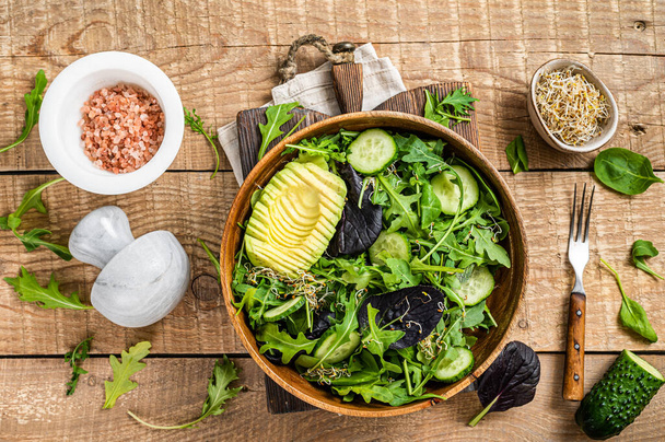 Grüner veganer Salat mit grünen Blättern, Avocado und Gemüse. Holzuntergrund. Ansicht von oben - Foto, Bild