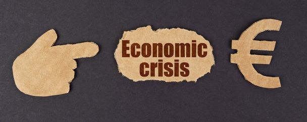 Economy and finance concept. On a black surface, a figure of a hand, a euro symbol and a torn cardboard with the inscription - economic crisis - Foto, Bild