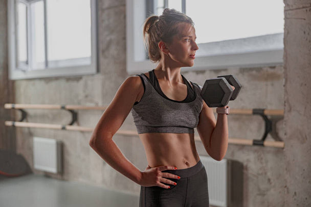 Sporty female athlete lifting dumbbell in gym - Photo, Image