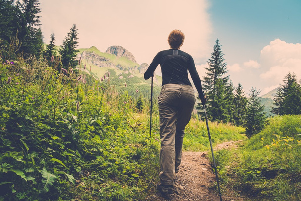 Mulher com caminhadas pólos andando na paisagem da montanha
  - Foto, Imagem