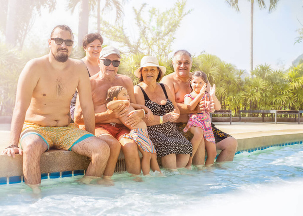 A large family of several generations sits on the side of the pool on vacation - Foto, imagen