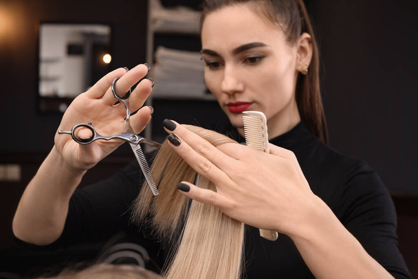 Professional hairdresser cutting woman's hair in salon, focus on hands - Fotografie, Obrázek