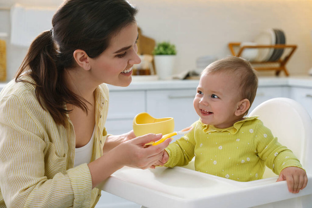 Mother feeding her cute little baby in kitchen - Фото, изображение
