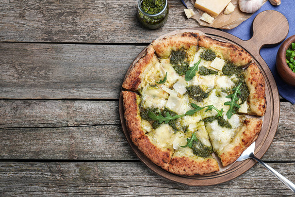 Delicious pizza with pesto, cheese and arugula served on wooden table, flat lay. Space for text - Фото, изображение