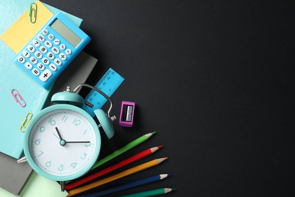 Flat lay composition with alarm clock and different stationery on black background, space for text. School time - Photo, Image