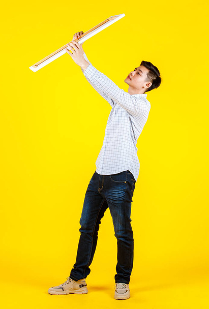 Portrait studio shot of Asian young handsome male businessman model in casual outfit standing smiling holding big white blank empty placard board for copy space advertising on yellow background. - Φωτογραφία, εικόνα