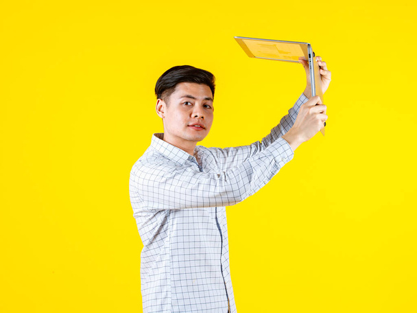 Portrait studio shot of millennial Asian young male businessman in casual outfit standing smiling holding laptop computer on yellow background - Fotó, kép