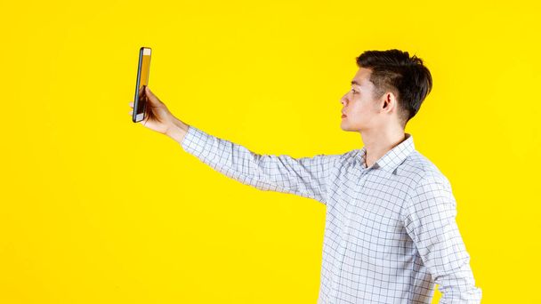 Портретная студия, изображающая молодого бизнесмена азиатского происхождения в повседневной одежде, улыбающегося, держащего ноутбук на желтом фоне - Фото, изображение