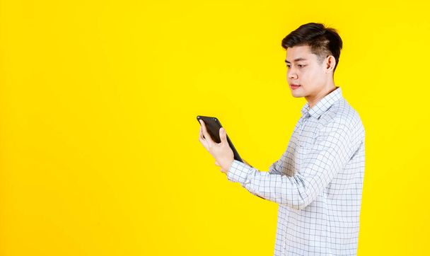 Portrait studio shot of millennial Asian young male businessman in casual outfit standing smiling holding laptop computer on yellow background - Photo, image