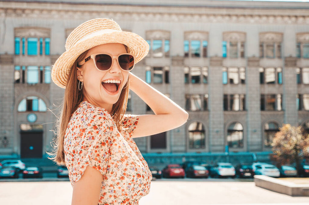 Young beautiful smiling hipster woman in trendy summer clothes. Sexy carefree woman posing on the street background at sunset. Positive model outdoors. Cheerful and happy in sunglasses and hat - Фото, зображення
