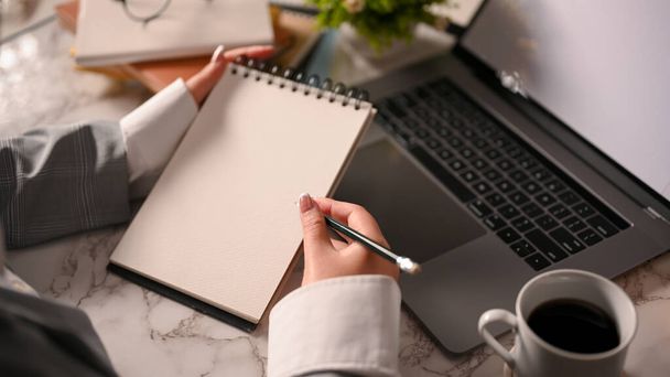 Una mujer de negocios elegante tomando notas en su bloc de notas en espiral sobre su escritorio de oficina moderno. primer plano - Foto, Imagen