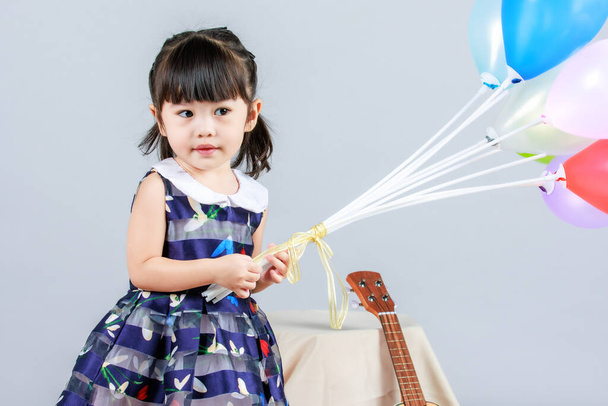 Portrait full body studio shot of little cute innocence kindergarten preschooler girl daughter in casual long blue dress standing smiling look at camera holding colorful balloons on gray background. - Photo, Image