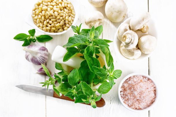 Branches of fresh oregano with leaves in a mortar, champignons, pink Himalayan salt, pine nuts, garlic and a knife on wooden board background from above - Φωτογραφία, εικόνα