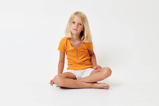 little girl with blond hair gesturing with her hands while sitting on the floor - Foto, Imagen