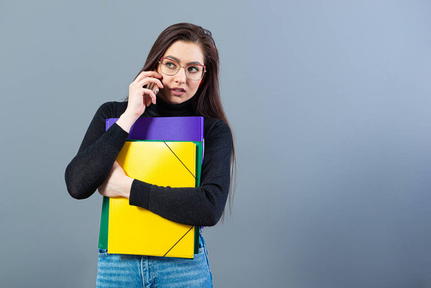 woman with smartphone holding a colorfuls folders with documents, isolated on dark background - Photo, Image