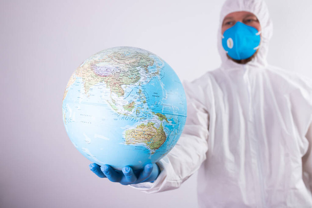 World epidemic danger concept. Male doctor man in medical face mask and gloves protecting planet Earth. - Fotoğraf, Görsel