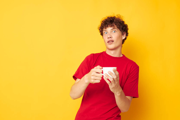 portrait of a young curly man in a red T-shirt with a white cap in his hands isolated background unaltered - Fotoğraf, Görsel