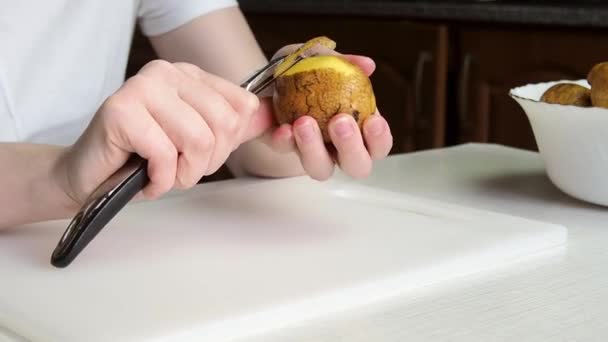 Egy fiatal lány keze, aki krumplit pucol. Házi készítésű étel főzése. - Felvétel, videó