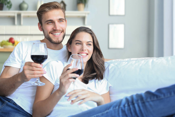 jong liefhebbend paar drinken een glas rode wijn in hun woonkamer - Foto, afbeelding