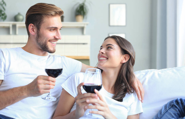 Młoda kochająca się para pije kieliszek czerwonego wina w salonie - Zdjęcie, obraz