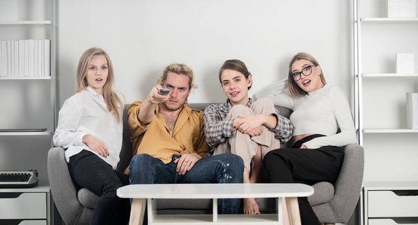 Youth group. Friends watching TV in evening at home. Group of young people sitting on sofa and talking at home. Young attractive people watch movies at home. - Foto, Bild