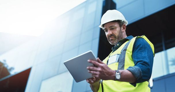 This software help me to keep track of everything. Shot of a engineer using a digital tablet on a construction site. - Foto, afbeelding