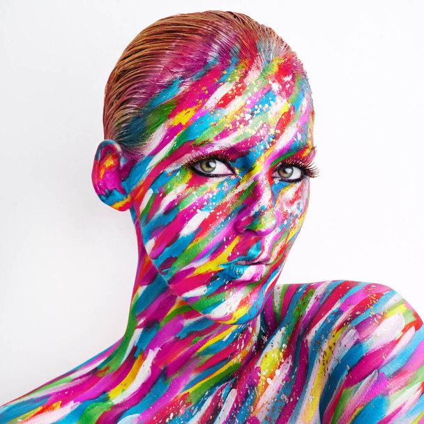 Theres art in beauty. Studio shot of a young woman posing with brightly colored paint on her face against a white background. - Foto, immagini
