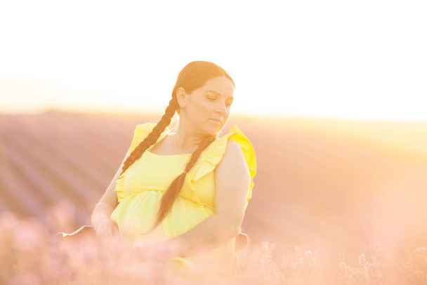 pregnant Woman in lavender flowers field at sunset in yellow dress. - Fotó, kép