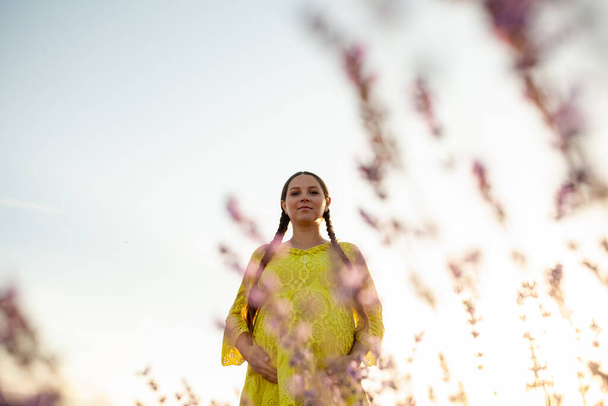 pregnant Woman in lavender flowers field at sunset in yellow dress. - Zdjęcie, obraz