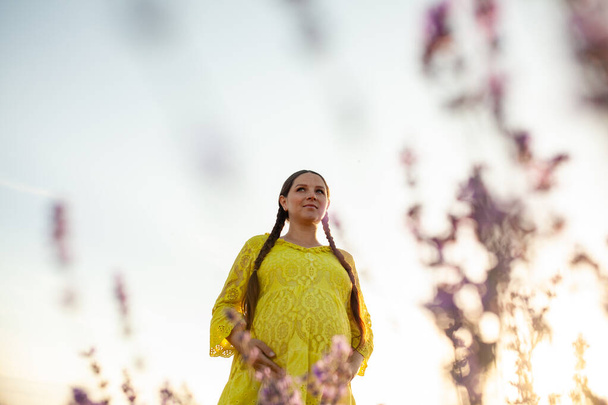 pregnant Woman in lavender flowers field at sunset in yellow dress. - Φωτογραφία, εικόνα