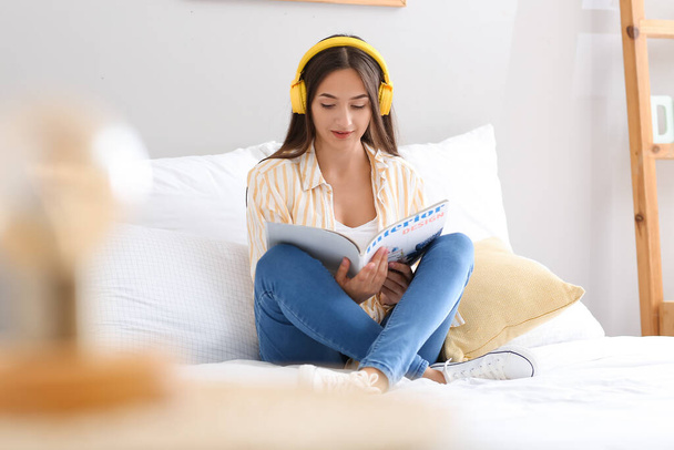 Pretty young woman listening to music and reading magazine at home - Фото, изображение