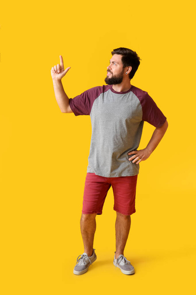 Knappe man in t-shirt wijzend naar iets op gele achtergrond - Foto, afbeelding
