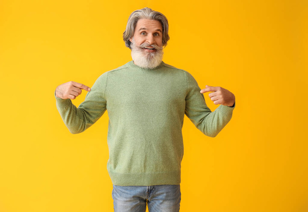 Handsome senior man in knitted sweater on yellow background - Photo, Image