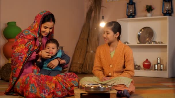 Een landelijke huisvrouw in saree kookt maaltijden voor haar familie in haar traditionele keuken. Een jong meisje spelen met haar zusje tijdens haar vrije tijd - Indiase dorpsscène, een gelukkig gezin, relatie en hechting, familie zorg - Video
