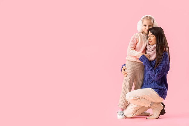 Little girl and her mother in warm sweaters hugging on pink background - Foto, immagini