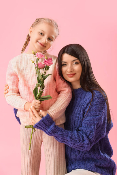 Маленька дівчинка з квітами і її мати в теплих светрах на рожевому фоні
 - Фото, зображення
