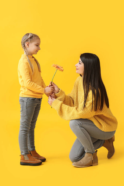 Маленькая девочка и ее мать с цветком на желтом фоне - Фото, изображение